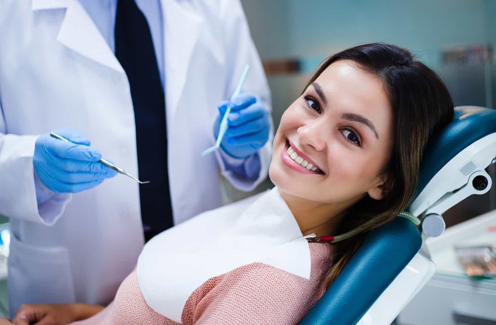 Happy young woman looking at camera as her dentist gets ready to begin her dental checkup