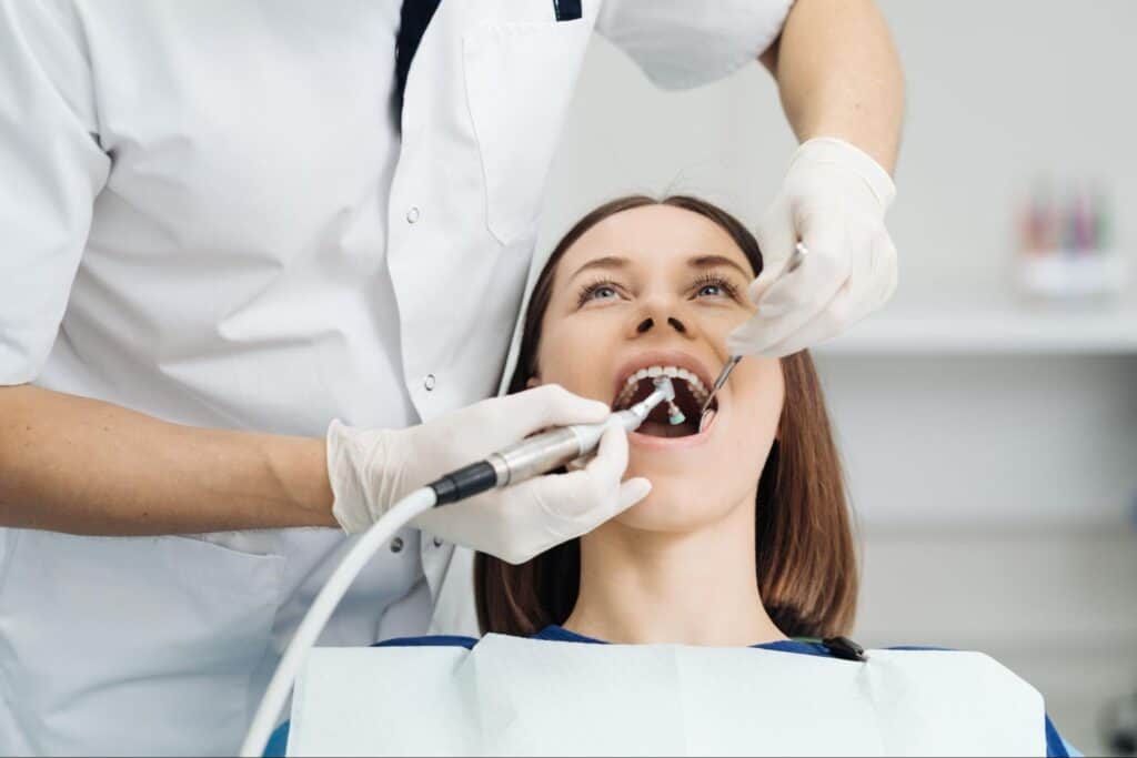 Alt text: A young patient is smiling during her dental scaling procedure.