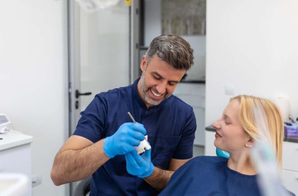 A smiling dentist using a plaster jaw model demonstrates to a sitting patient where a bridge could take place.