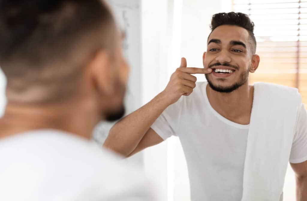 A young adult smiling and examining his teeth in the mirror trying to tell if his gums are receding.