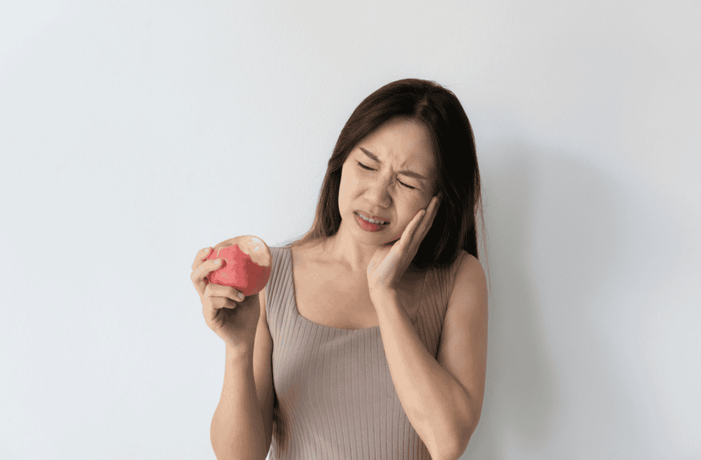 A person holds their cheek in pain after biting an apple.