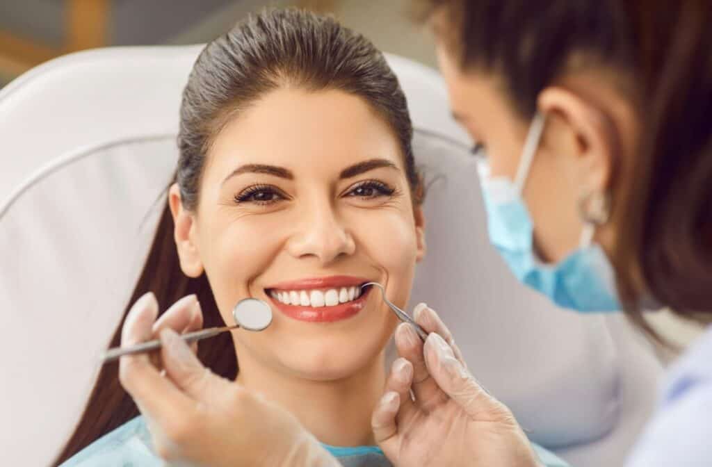 An adult patient smiling big revealing a white and healthy smile while a dentist uses tools to ensure teeth are healthy.
