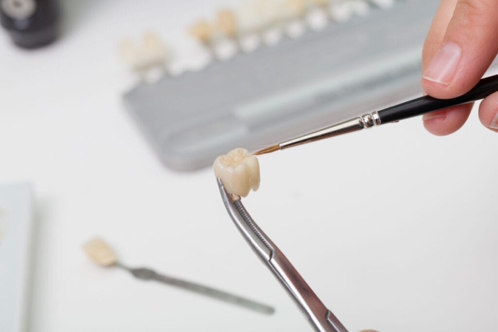 Dental technician applying finishing touches to a ceramic dental crown restoration using precise dental laboratory tools.
